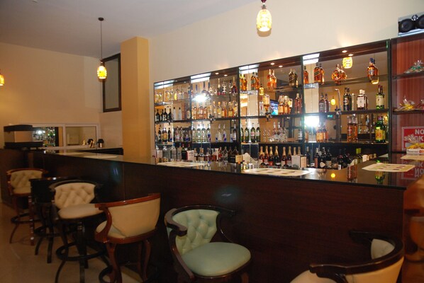 A bar area with multiple liquor bottles, bar stools, and hanging light fixtures. - Churchill Hotel (Addis Ababa)
