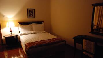 A hotel room with a bed, a nightstand with a lamp, a framed picture on the wall, and a chair.