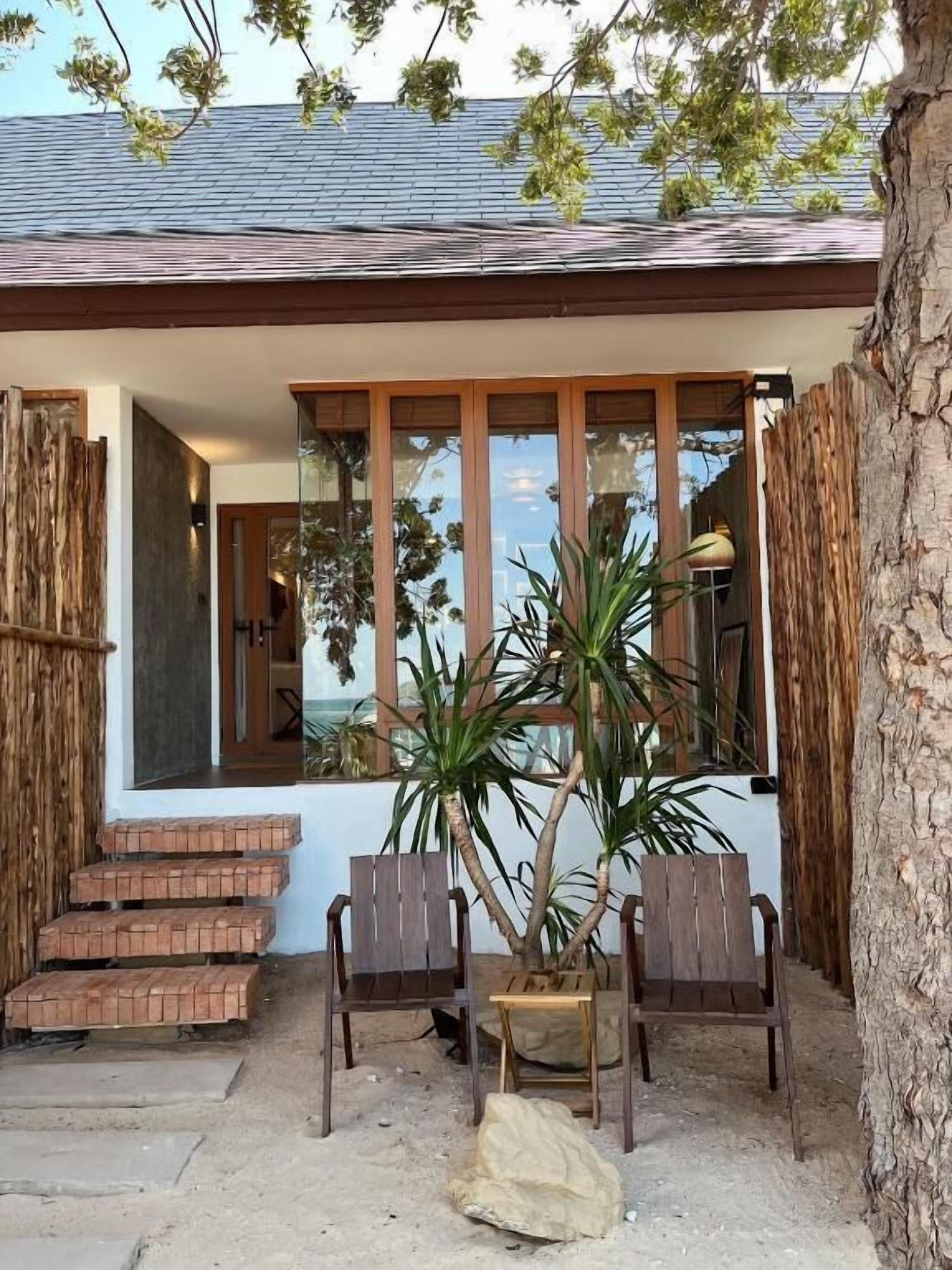A coastal house with a wooden deck, two chairs, and a large potted plant.