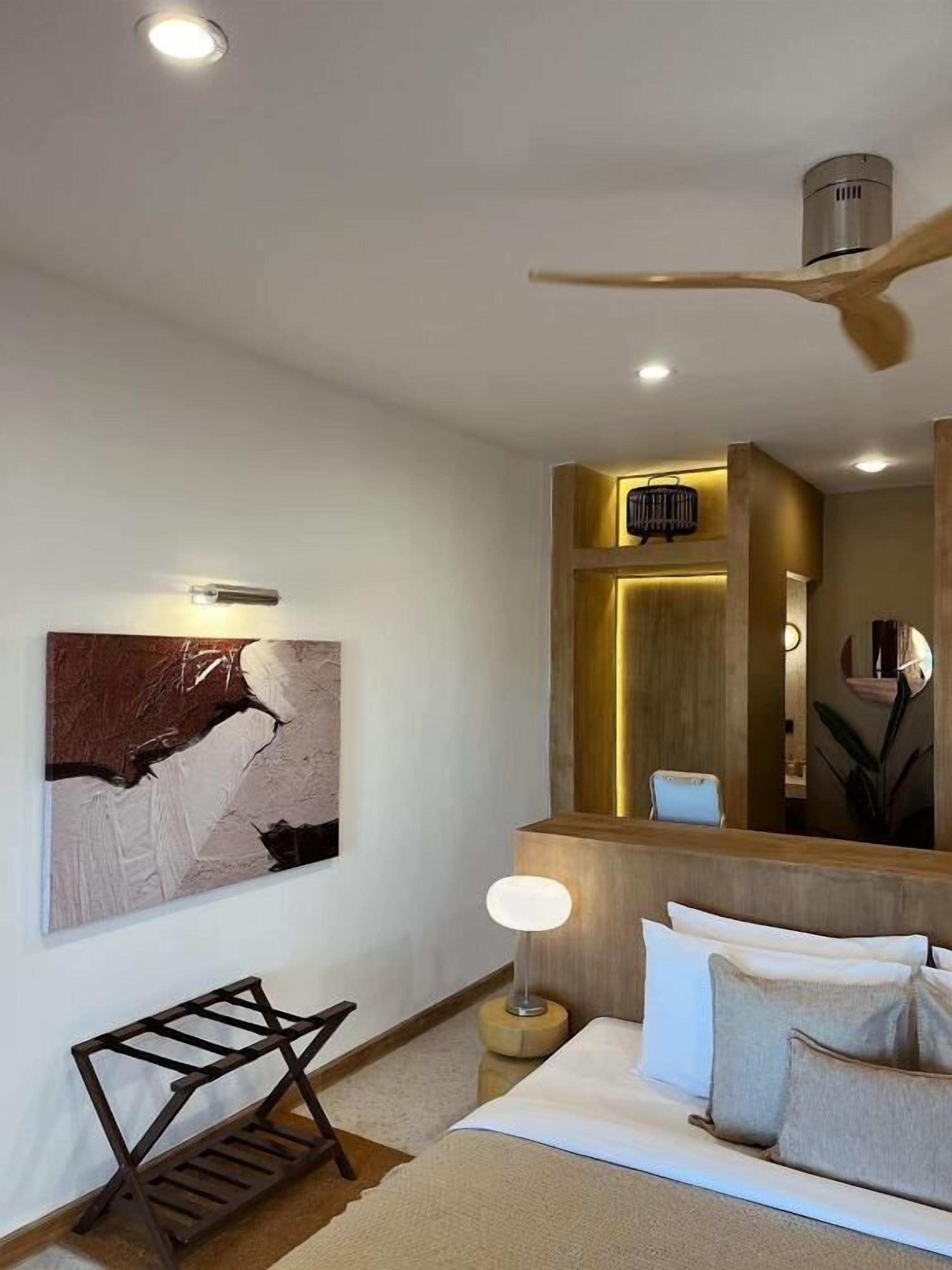 A modern hotel room with a bed, bedside table, lamp, and a large abstract painting on the wall.