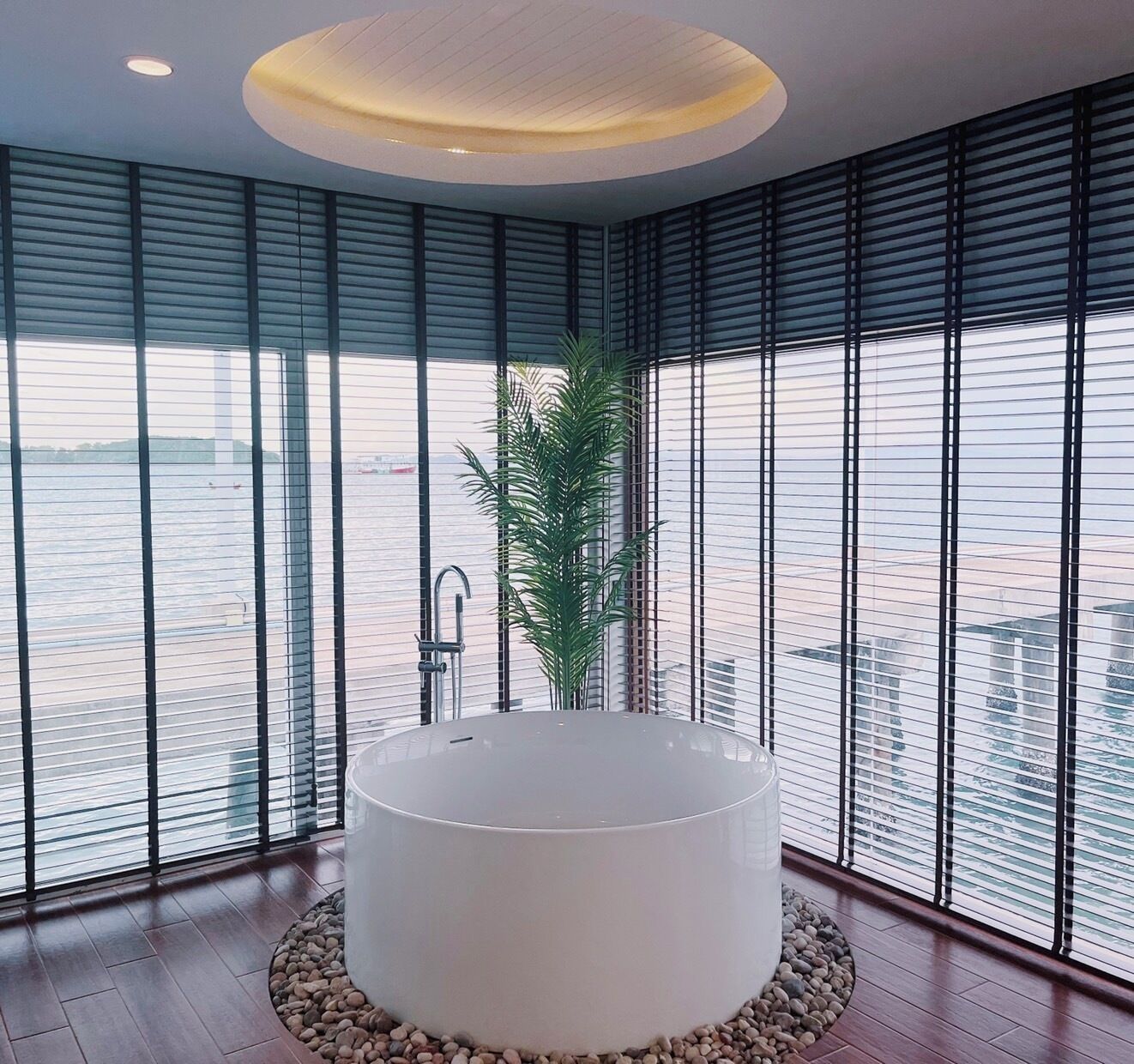A modern bathroom with a large bathtub, a potted plant, and a view of the water outside.