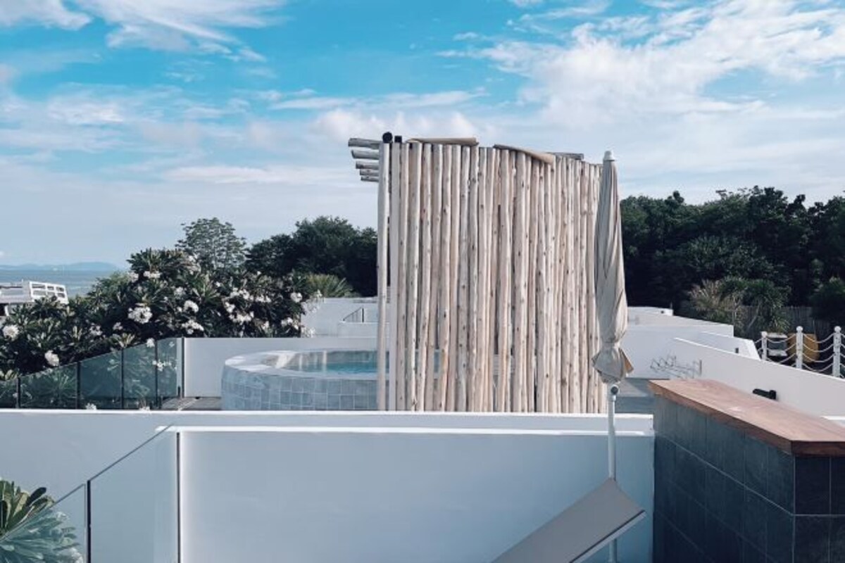 A rooftop terrace with a pool, a wooden fence, and a view of the landscape.