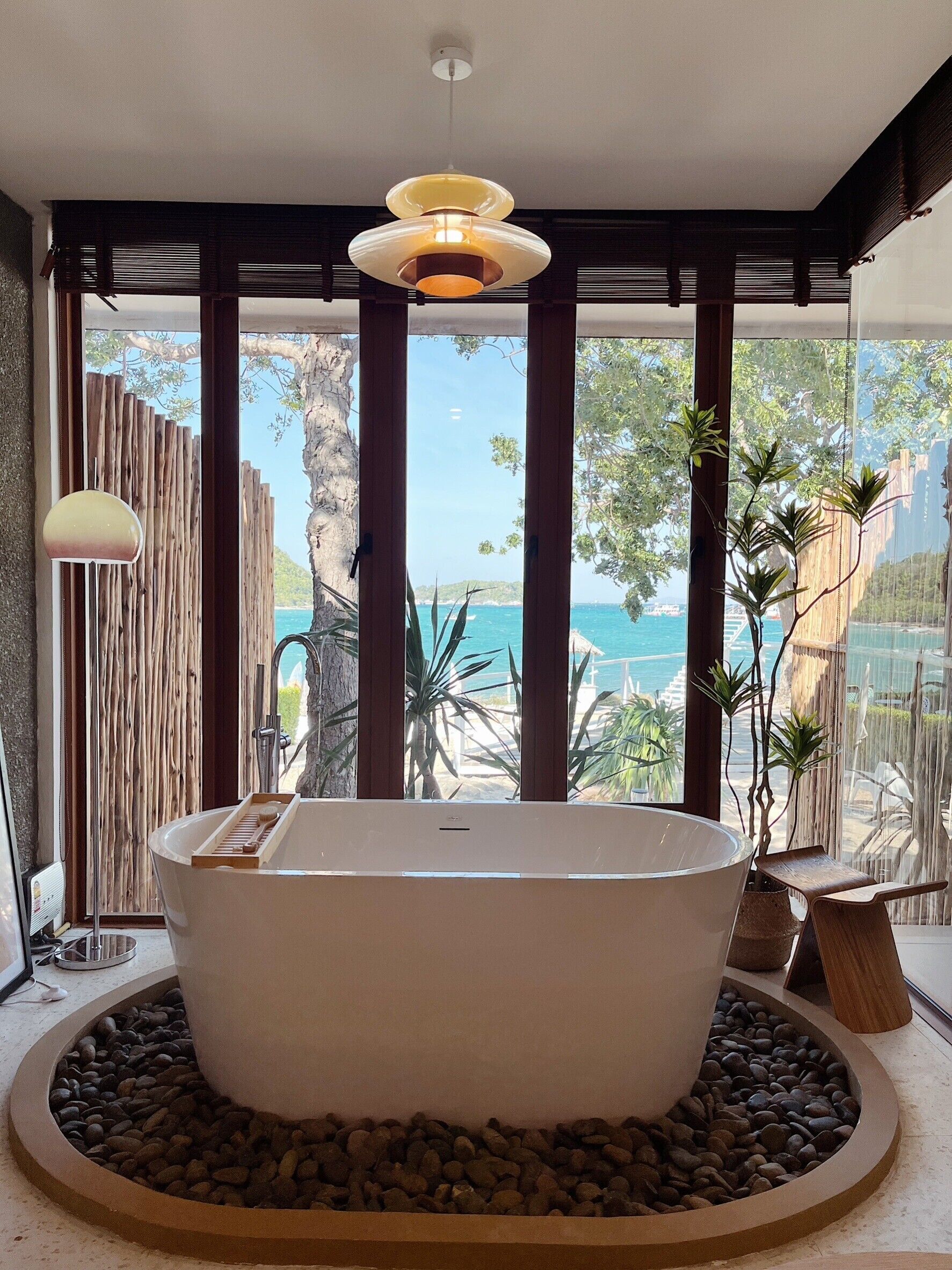A modern bathroom with a freestanding bathtub, large windows, and a view of the sea.