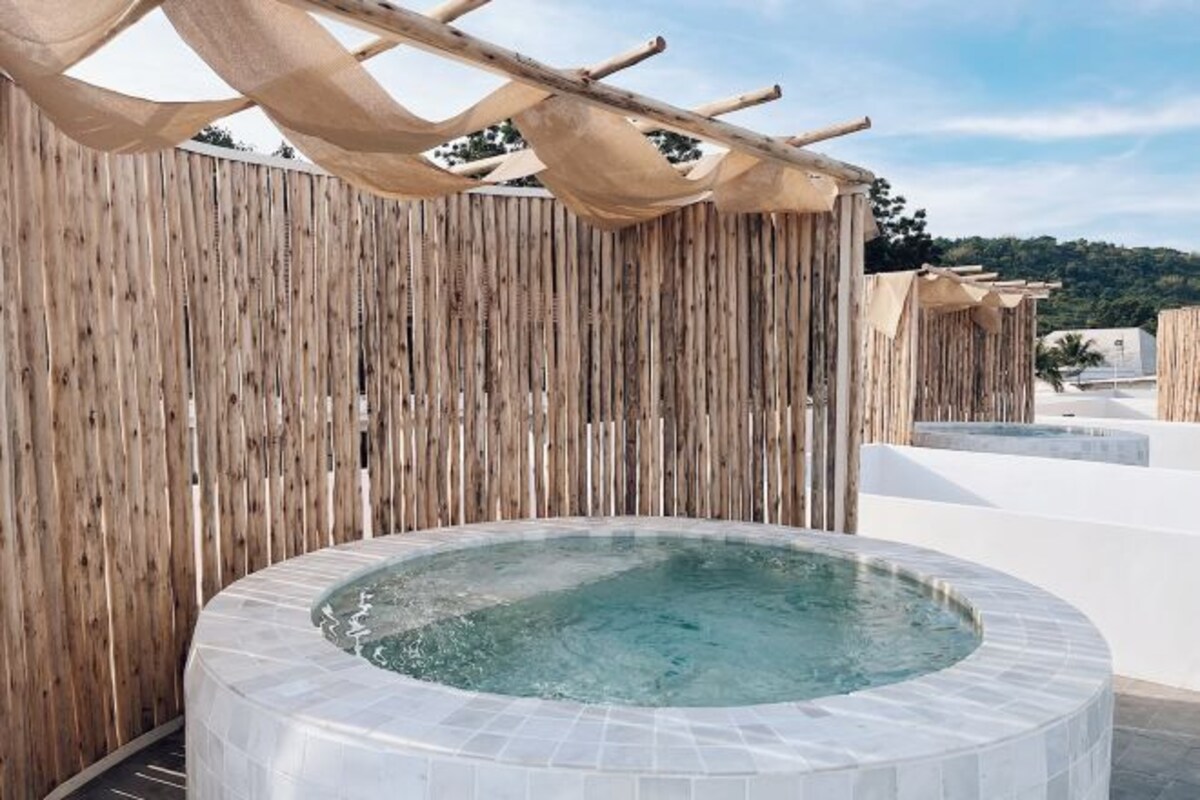 A hot tub with a wooden fence backdrop and a pergola overhead.