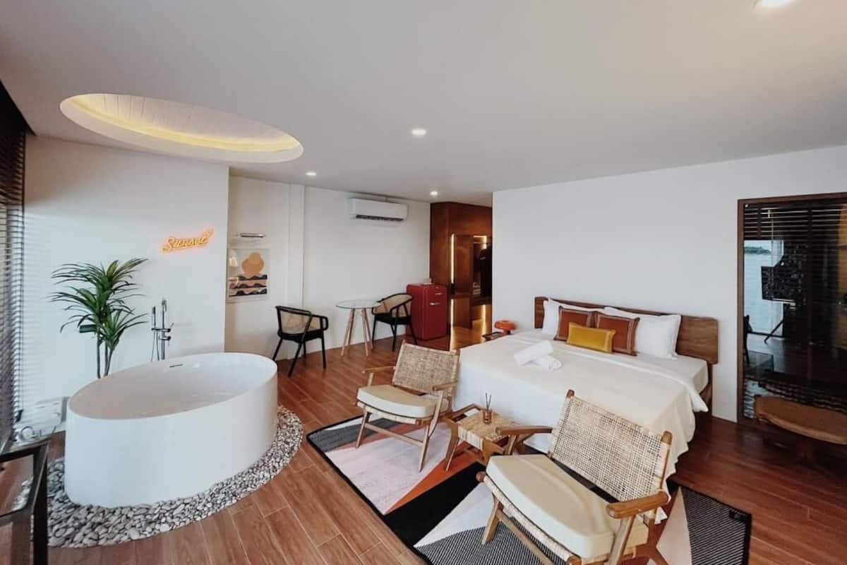 Una habitación de hotel moderna con una cama grande, una zona de estar con sillas, una bañera y una pequeña mesa.