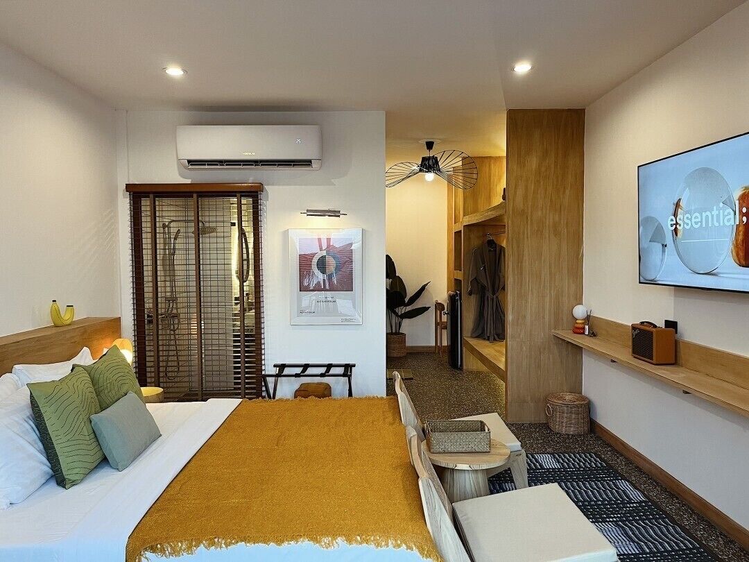 Ein Hotelzimmer mit Bett, Schreibtisch, Sessel, Klimaanlage, Kleiderschrank, Fernseher und einem gerahmten Bild an der Wand.