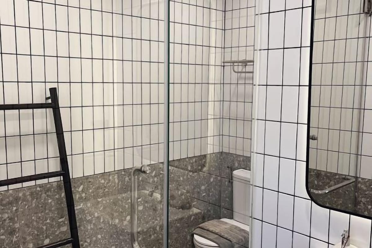 A bathroom with white tiled walls, a marble floor, a shower, and a toilet.