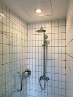 Un baño moderno con paredes de azulejos blancos, cabina de ducha de vidrio y un cabezal de ducha de mano.