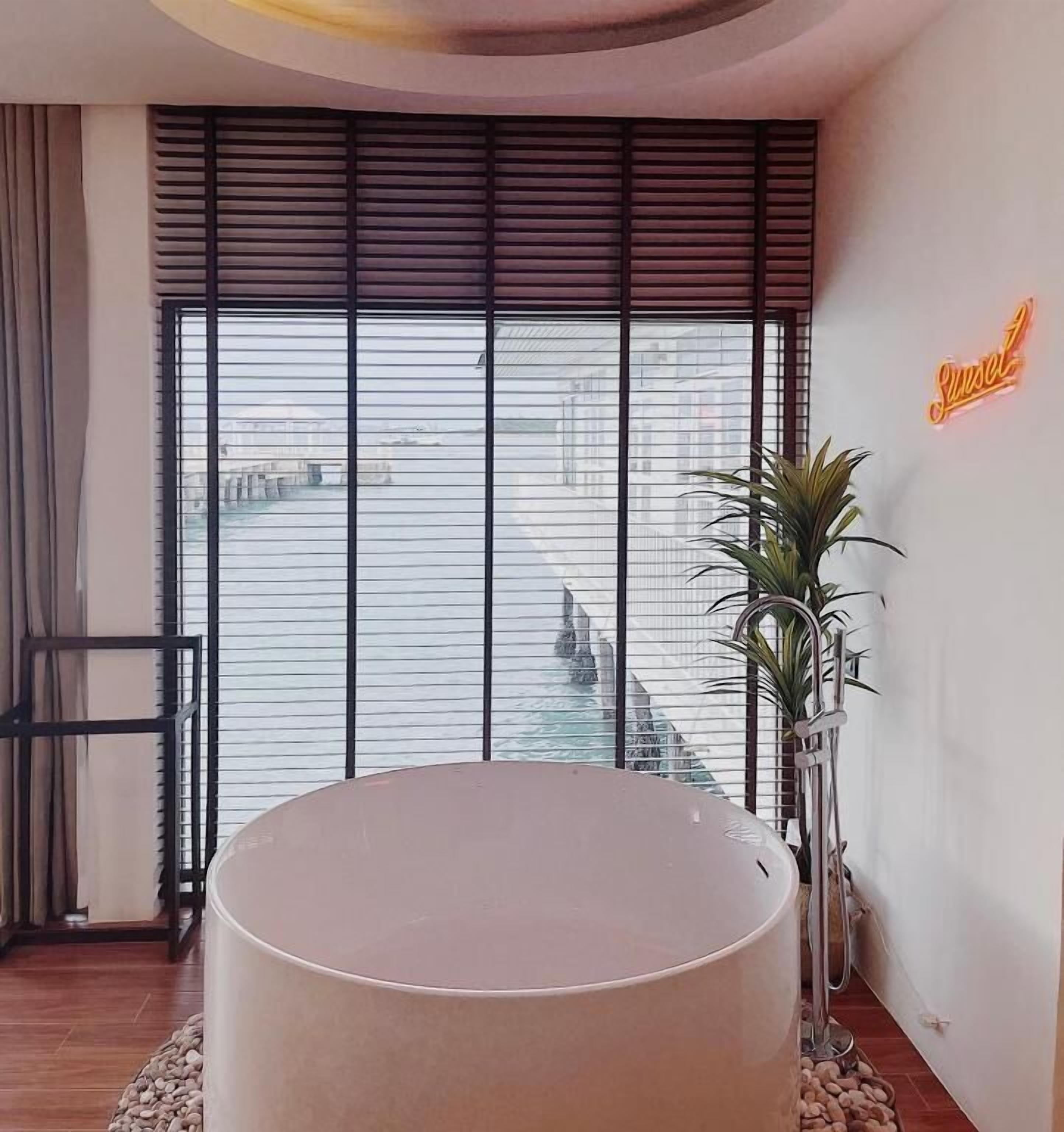 Une salle de bain moderne avec une grande baignoire, une plante en pot et un panneau lumineux au néon.