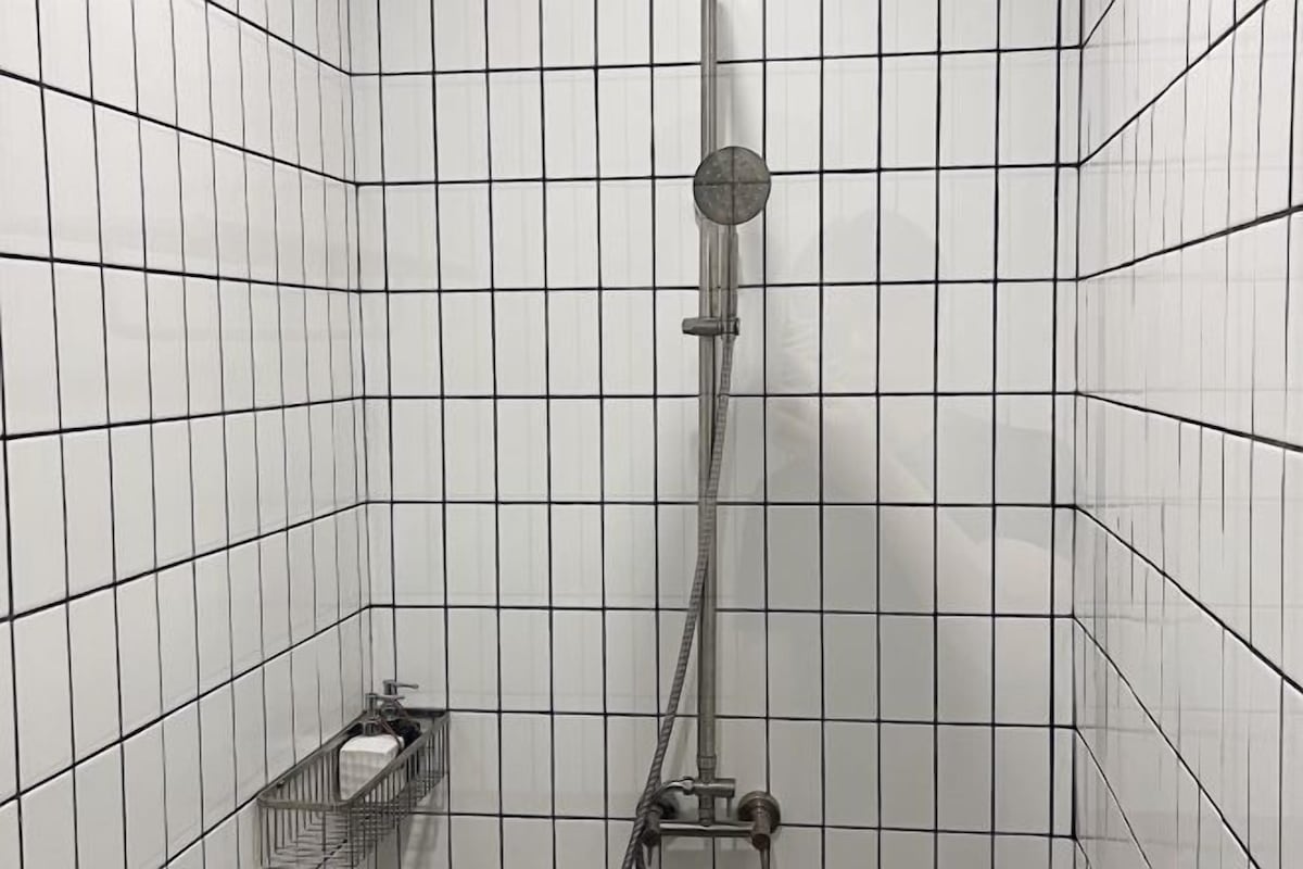 A tiled shower stall with a handheld showerhead and a wall-mounted faucet.