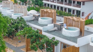 Hotel modern amb diverses banyeres d'hidromassatge a la terrassa, envoltat de vegetació exuberanta i una tanca de fusta.