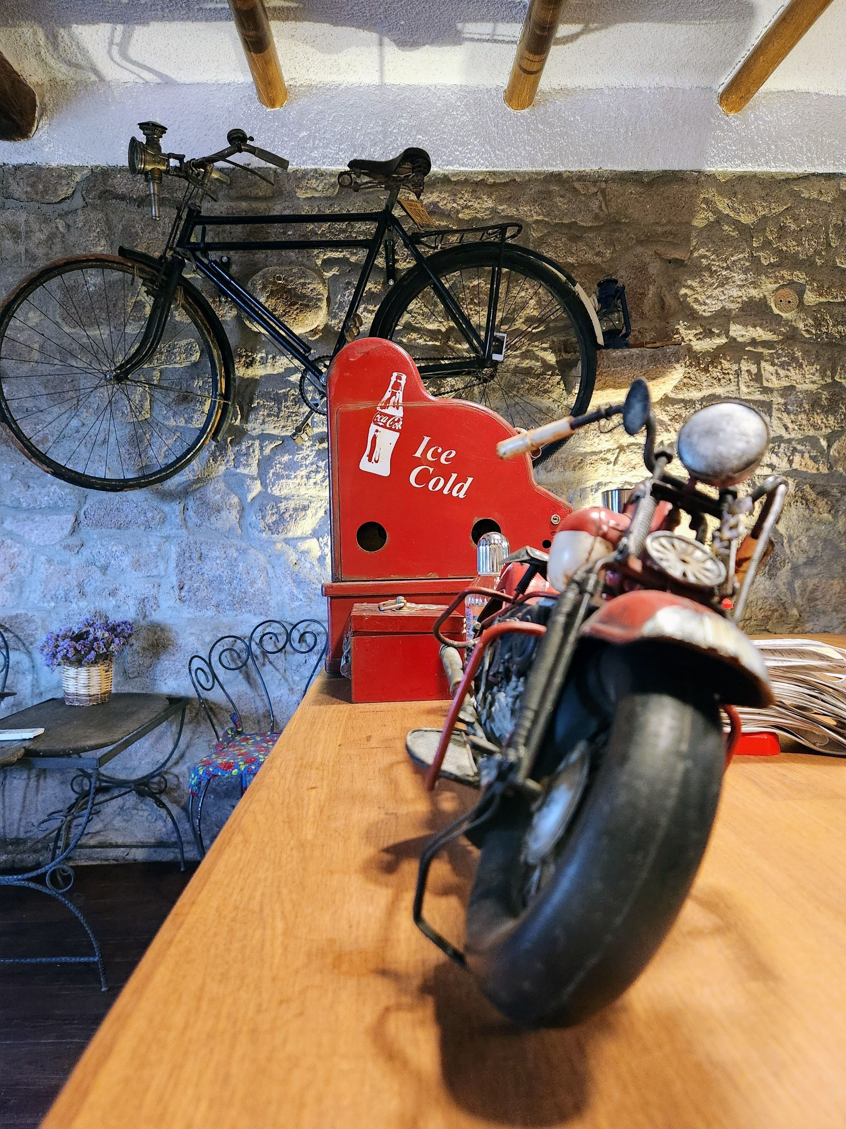 A vintage motorcycle with a red Coca-Cola logo, a bicycle, and a stone wall in the background.