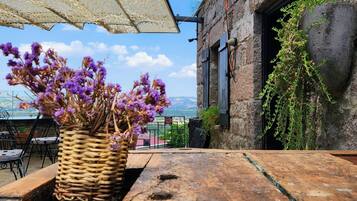 Un área de estar al aire libre con una mesa de madera rústica, una cesta de mimbre con flores moradas y una pared de piedra con un farol colgante.