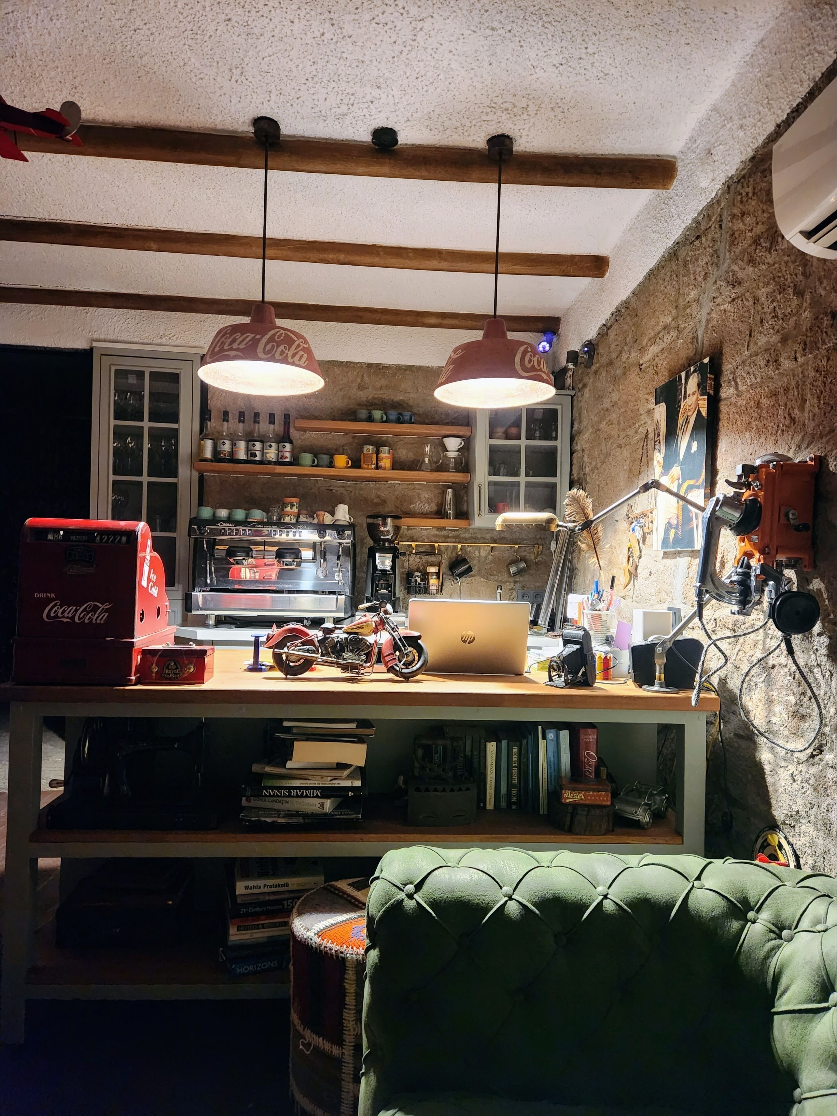 Un espacio de trabajo acogedor con un escritorio de madera, una computadora portátil, una motocicleta y un refrigerador vintage de Coca-Cola.