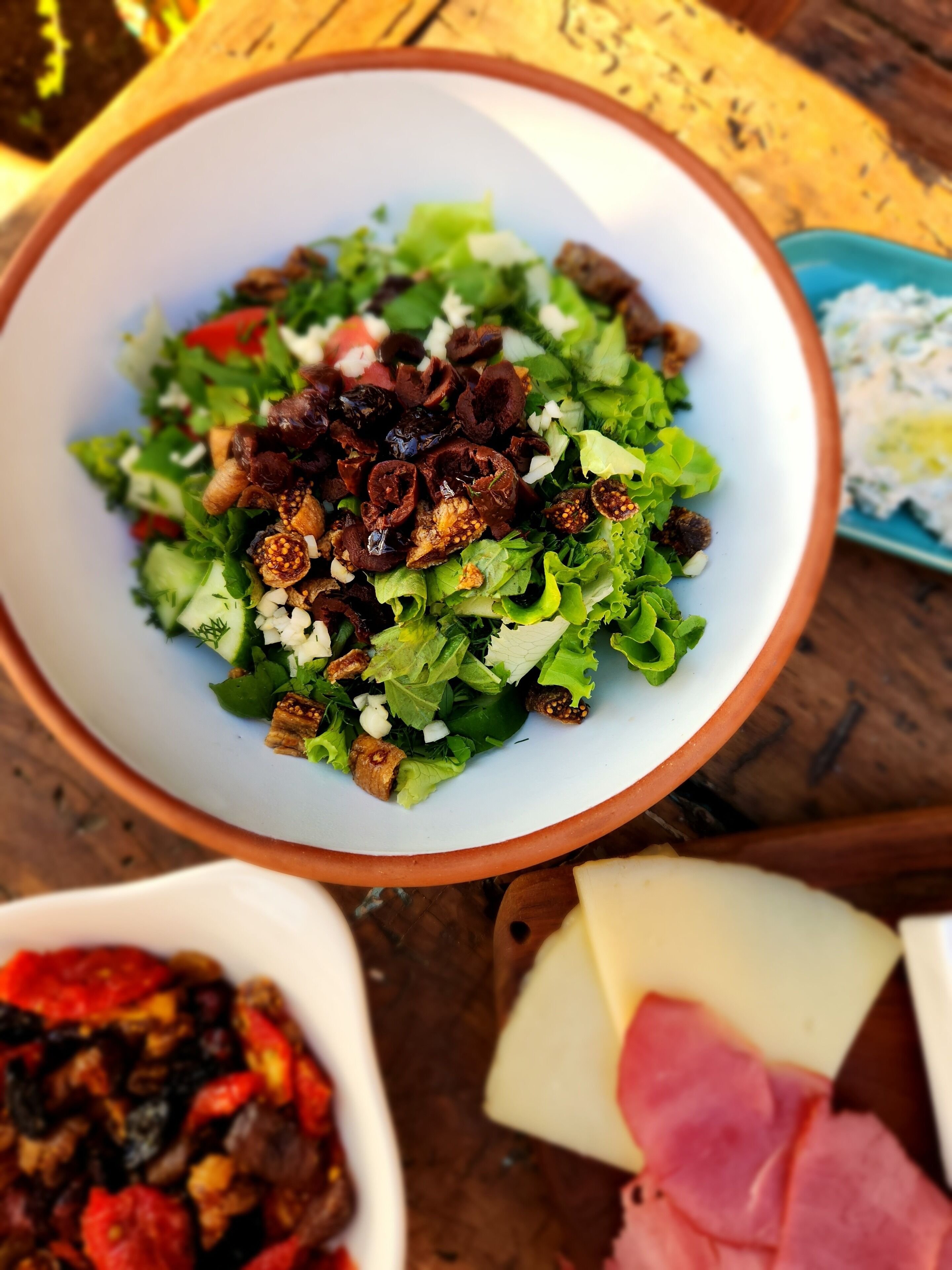 Un tazón de ensalada con diversos ingredientes, un plato de queso y un recipiente que parece contener una salsa o aderezo.