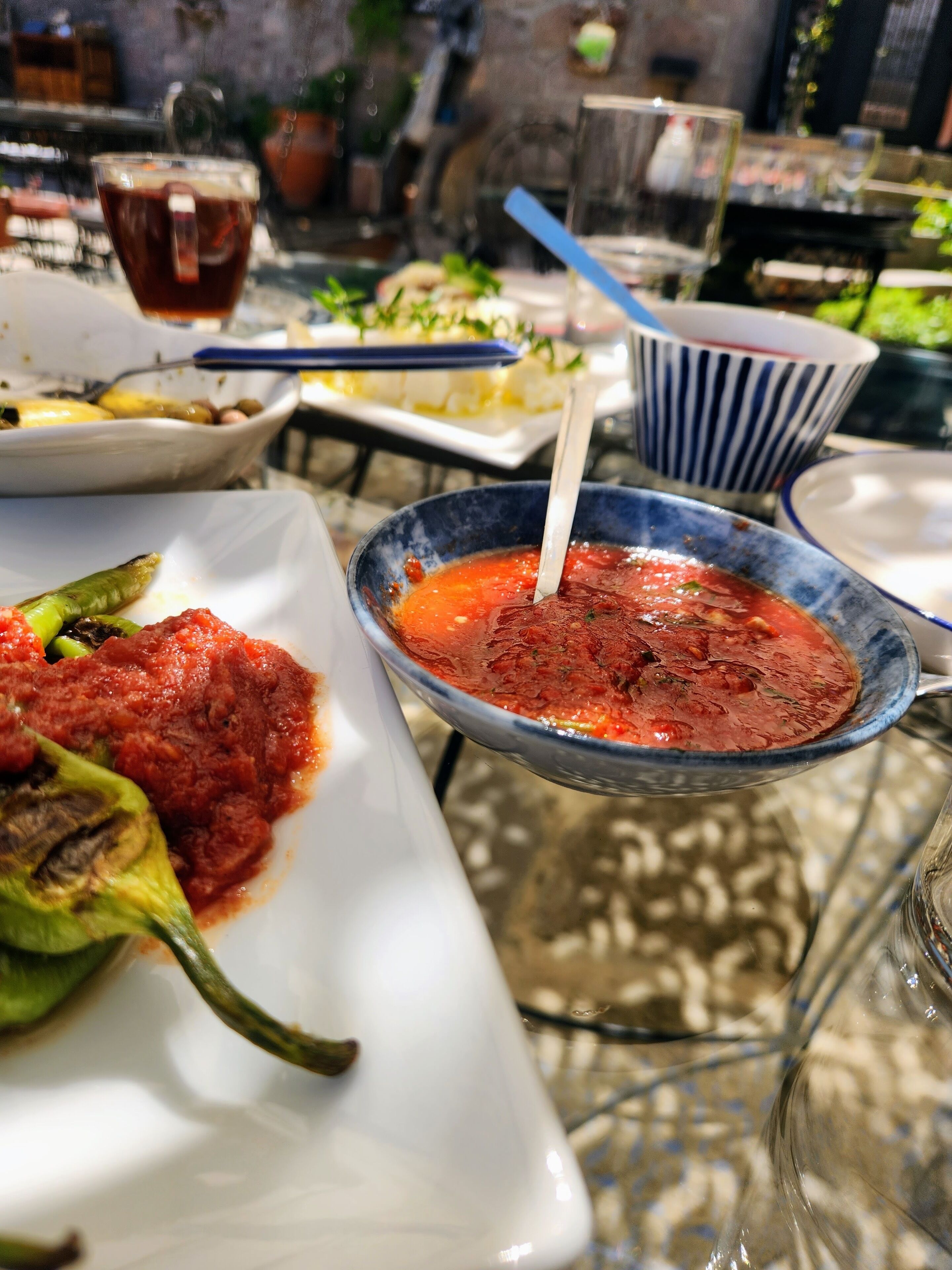 A dining table with various dishes, including a bowl of red sauce and a plate with a green vegetable.