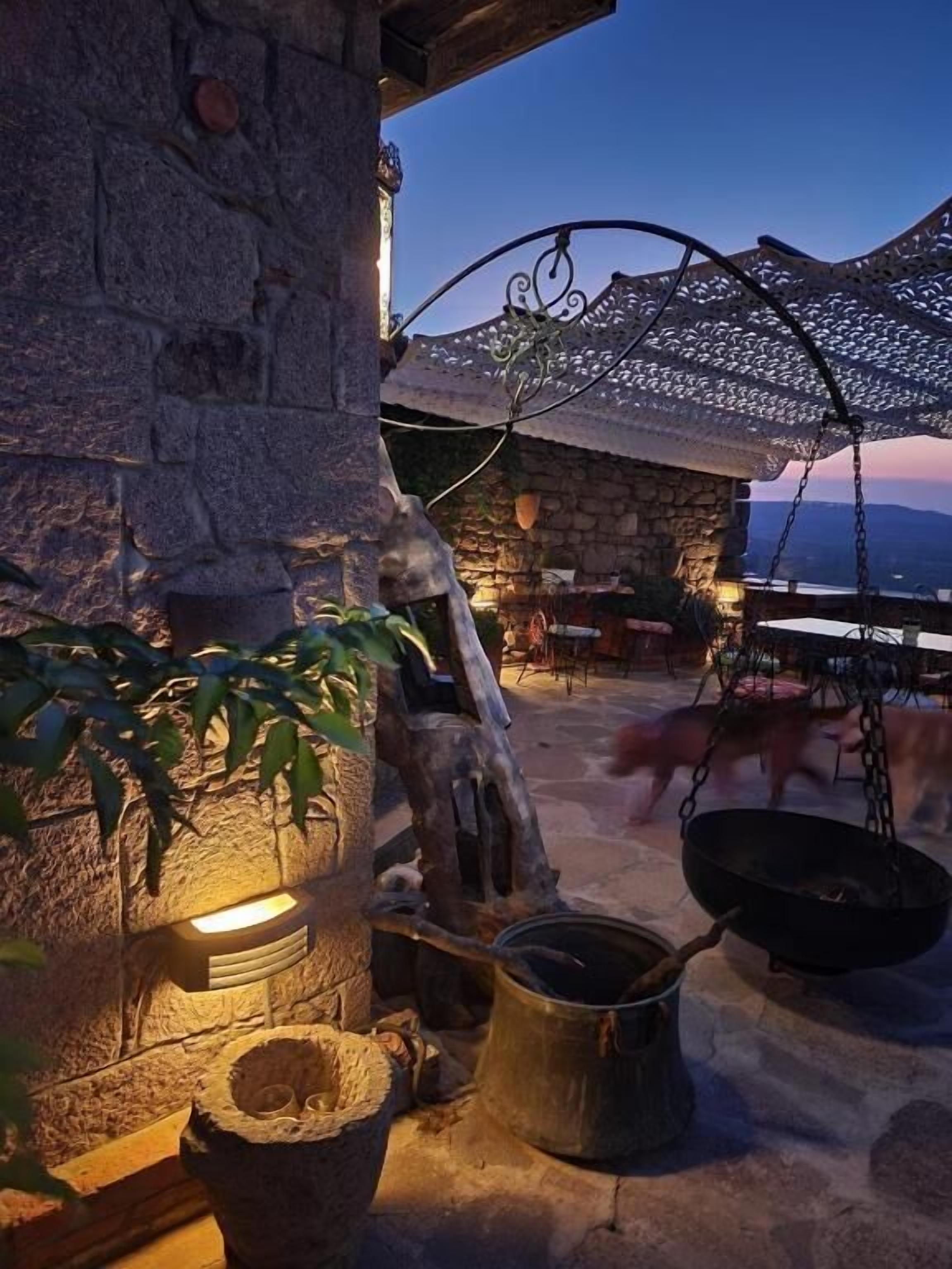 A rustic outdoor setting with stone walls, a hanging chair, and a fire pit.