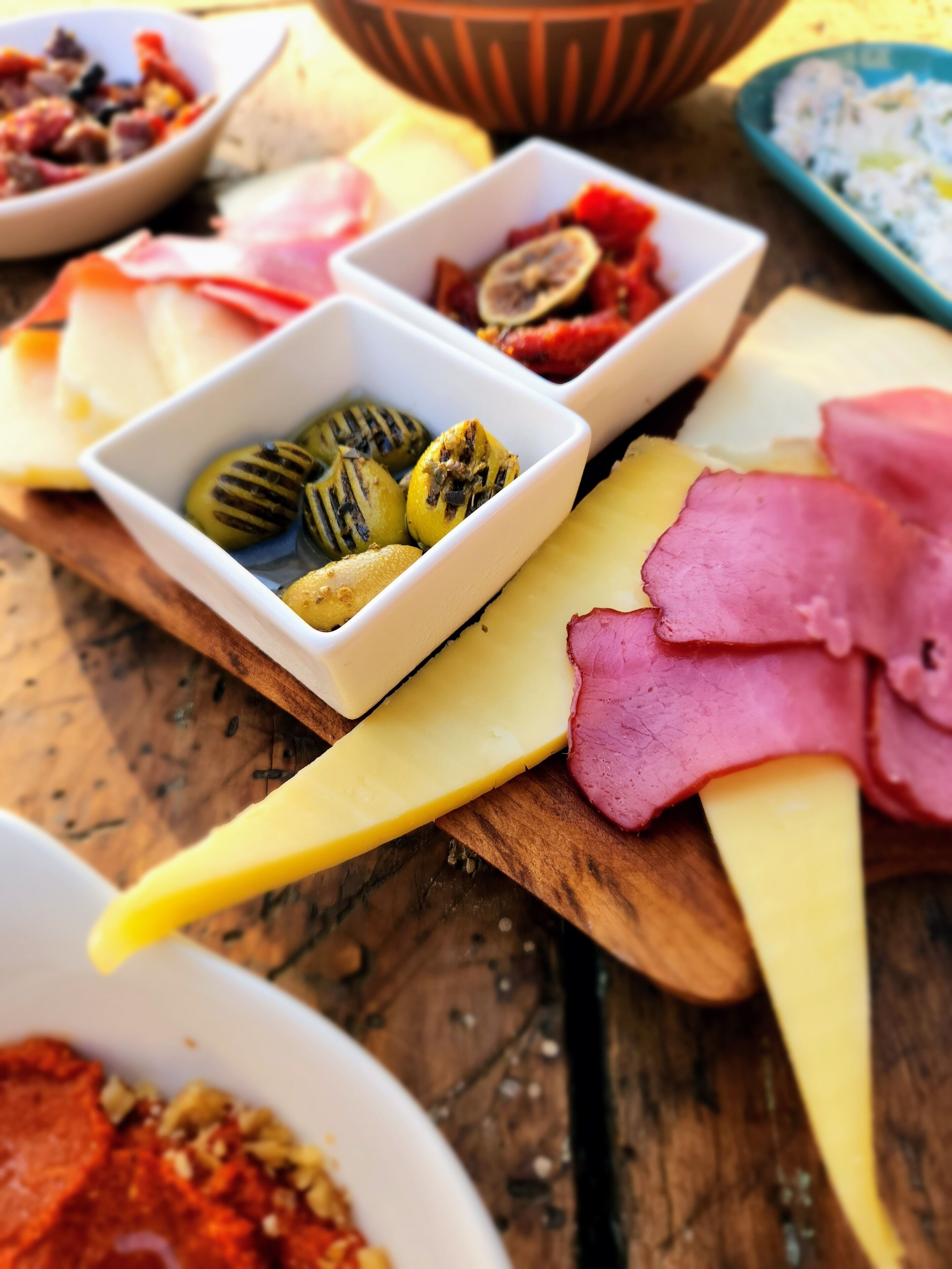A wooden board with various cheeses, cured meats, and olives.