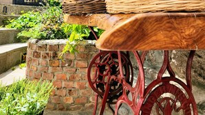 A rustic outdoor setting with a wooden table supported by ornate metal legs, a brick wall, and a stone wall in the background. -  Assos Sunset Boutique Hotel (Ayvacik)