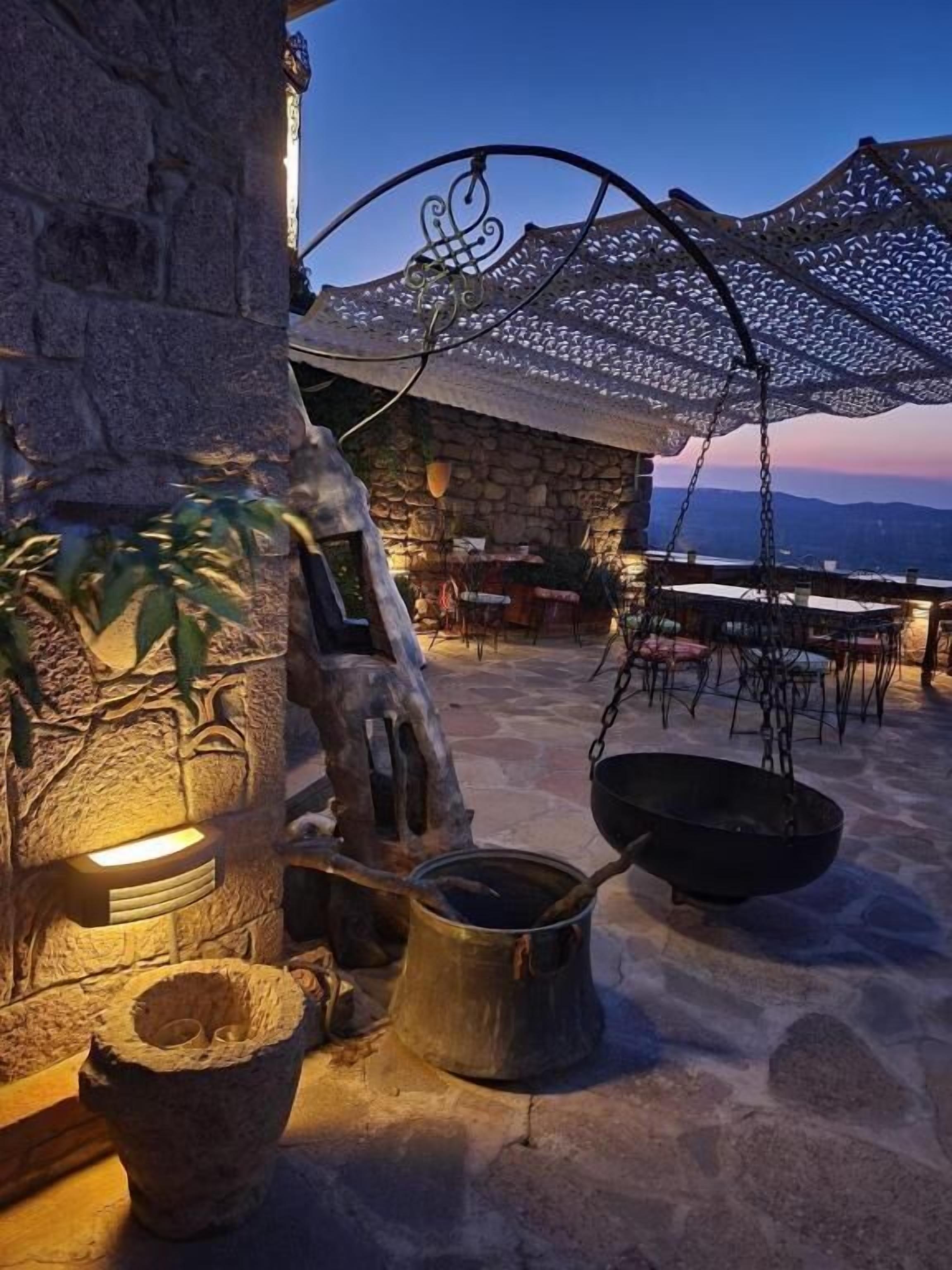 Un área de estar al aire libre con paredes de piedra, una parrilla metálica colgante y vistas al paisaje.