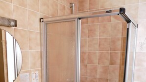 A bathroom with a beige tiled wall, a sink with a mirror, and a glass-enclosed shower. - Zum Mühlehannes (Sankt Ingbert)