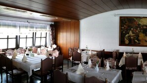 A restaurant with multiple tables set for dining, a large painting on the wall, and wooden paneling on the ceiling. - Zum Mühlehannes (Sankt Ingbert)
