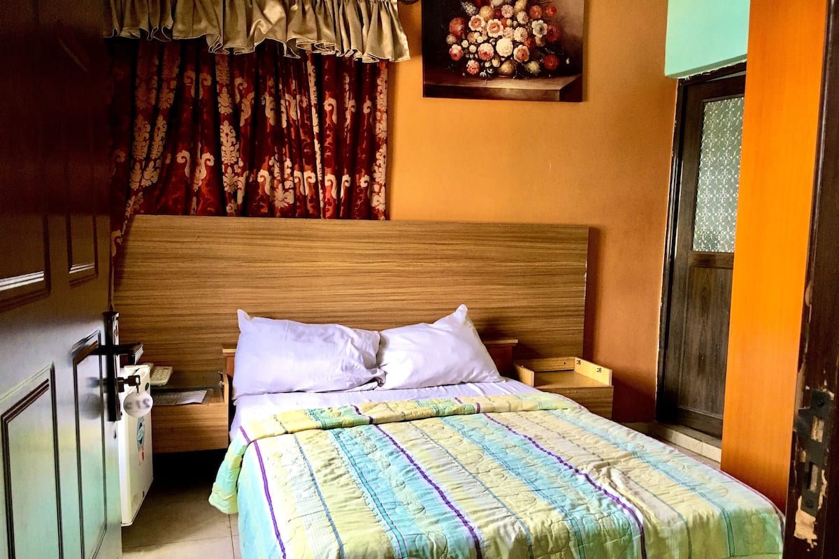 A bedroom with a wooden headboard, a bed with a colorful quilt, a bedside table, and a nightstand.