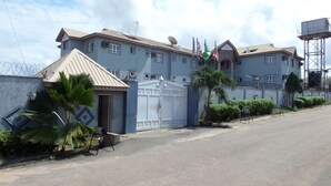 A large, multi-story building with a gated entrance, satellite dish, and multiple flags. - Indices Hotel and Garden (Abeokuta)