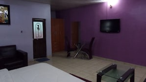 A room with a bed, a TV mounted on the wall, a bicycle, and a door with a poster. - Indices Hotel and Garden (Abeokuta)