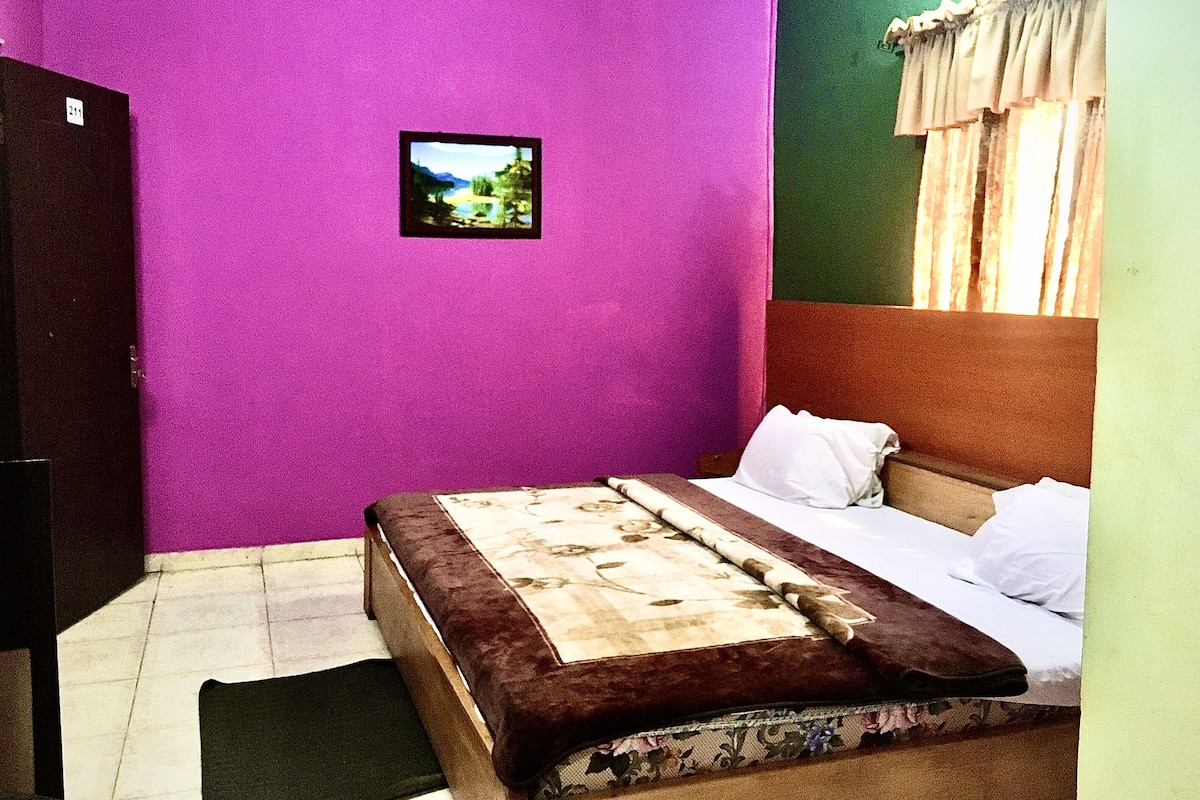 A bedroom with a purple wall, a bed with a floral bedspread, and a small picture on the wall.