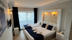 Une chambre d’hôtel moderne avec deux lits, une grande fenêtre, un téléviseur à écran plat, une table de chevet avec une lampe et une télécommande posée sur une petite table.