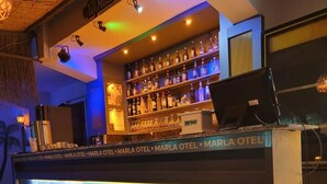 Un espace bar avec une fresque représentant une sirène sur le comptoir, des étagères remplies de bouteilles et une enseigne indiquant « MARLA OTEL ».