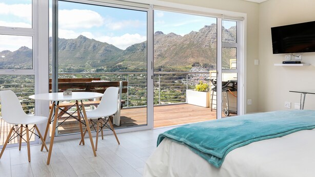 A bedroom with a large window, a bed, a TV, and a balcony with a table and chairs. - Mount Bay (Cape Town)