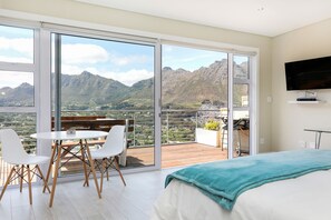 Un dormitorio con un ventanal grande, una cama, un televisor y un balcón con una mesa y sillas.