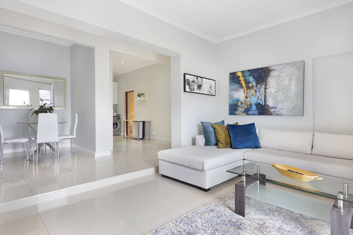 Una sala de estar moderna con una mesa de centro de vidrio, un sofá blanco y arte abstracto en la pared.