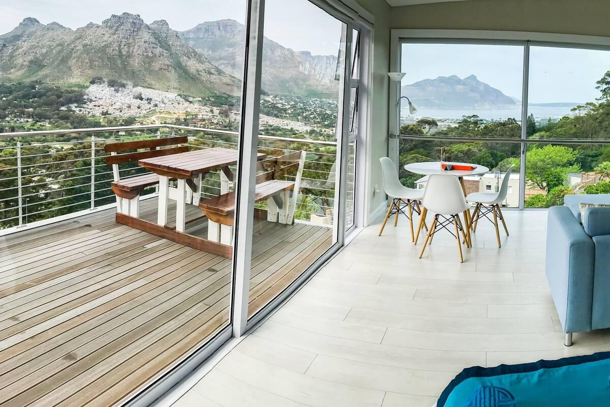 Un salón moderno con sofá, una mesa de comedor con sillas y un balcón con terraza de madera.