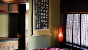 Una habitación tradicional japonesa con suelo de tatami, cama de madera baja, pantalla shoji y un pergamino colgante con caligrafía.