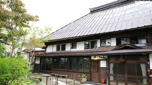 Un edificio tradicional japonés con tejado de tejas, ventanas grandes y entrada de madera.