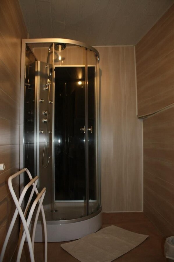 Un baño moderno con ducha de vidrio, una silla blanca y piso de madera.