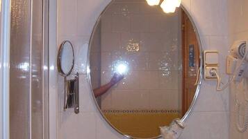 Une salle de bain avec un miroir rond, un lavabo et une douche.