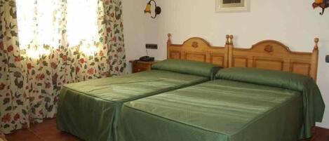 A double bed with green bedding, a floral curtain, a small bedside table, and a wall-mounted lamp.