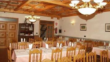 Un comedor con mesas y sillas de madera, una araña y un techo con vigas a la vista.