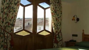 A room with a large bay window, floral curtains, and a bed with a green bedspread. - Hostal Las Grullas (Tornos)