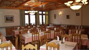 A dining area with multiple tables and chairs, wooden ceiling beams, and large windows with curtains. - Hostal Las Grullas (Tornos)