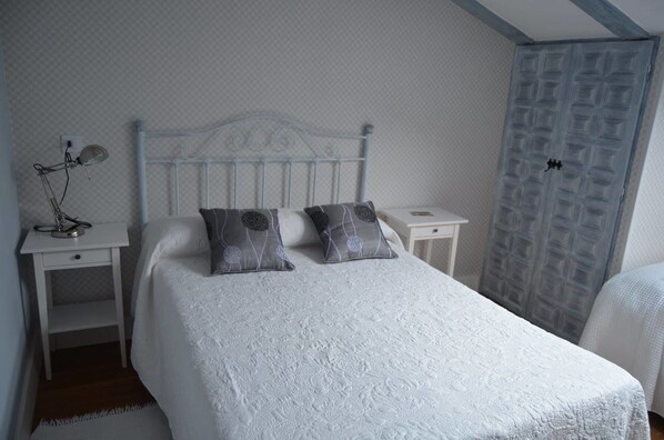 A bedroom with a white bed, two pillows, a nightstand with a lamp, and a wardrobe with a geometric pattern.