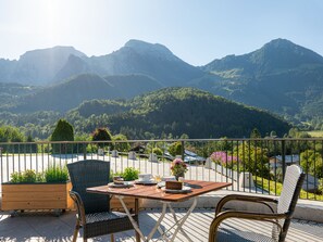 A terrace with a table and chairs, overlooking a mountainous landscape. - Hotel Garni Hanauerlehen (Schoenau am Koenigssee)