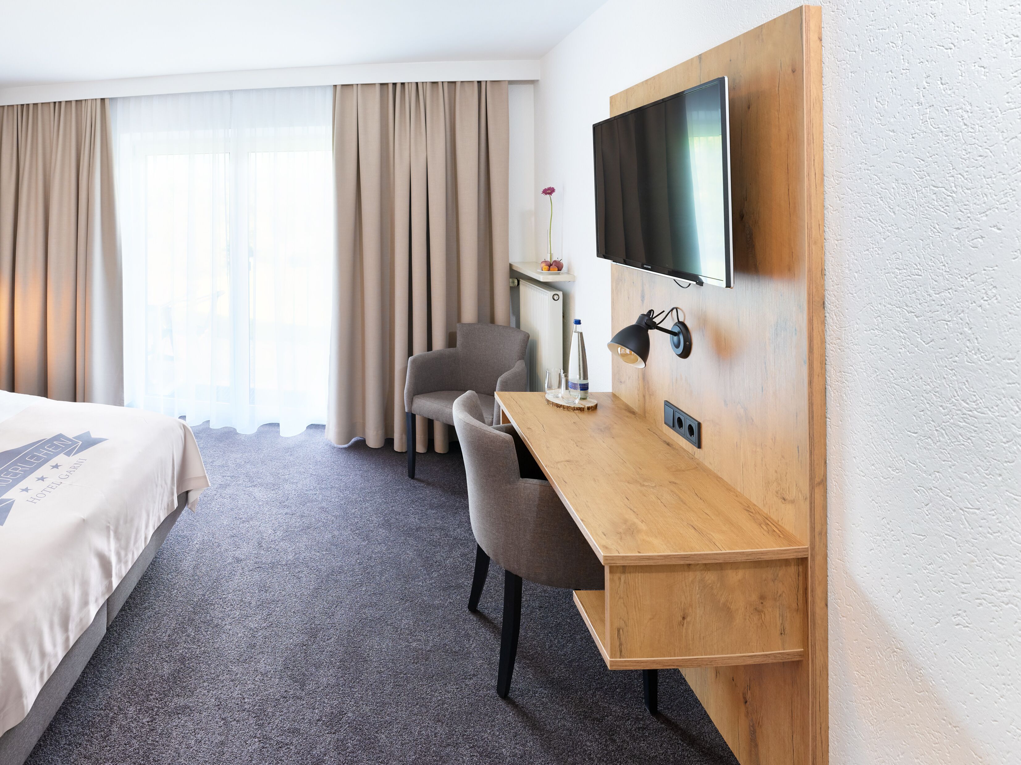 Ein Hotelzimmer mit einem Bett, einem Schreibtisch, einem Stuhl, einem Fernseher und einem fenster mit Vorhängen.