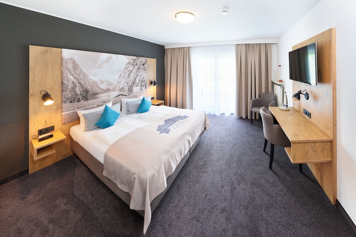 A hotel room with a large bed, a desk, a chair, and a TV.
