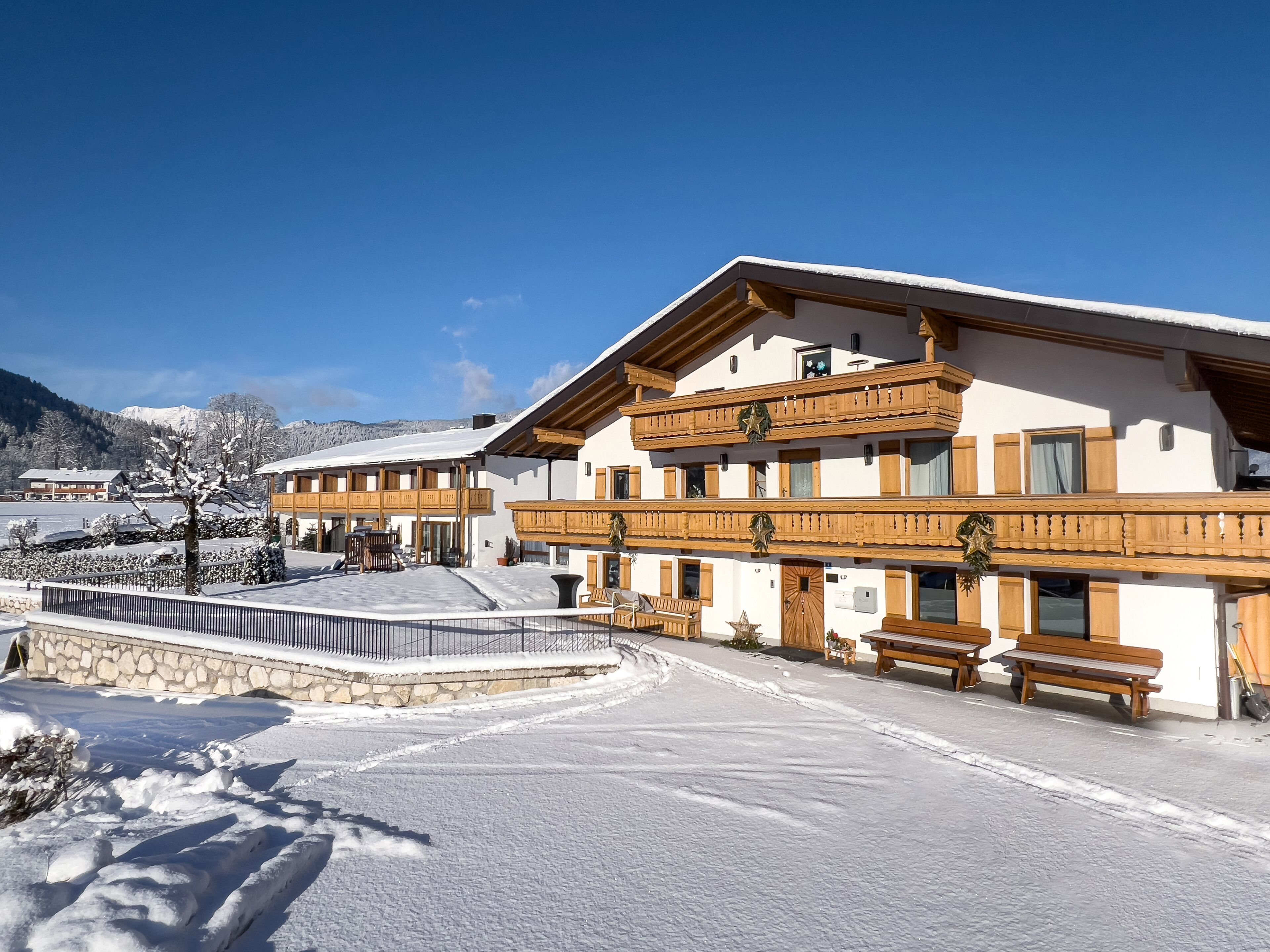 A multi-story building with wooden balconies, a stone wall, and a snow-covered ground.