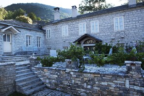 A stone building with a stone staircase leading to a door, a garden with grapevines, and a mountain in the background. - Amaryllis Boutique Guest House (Zagori)